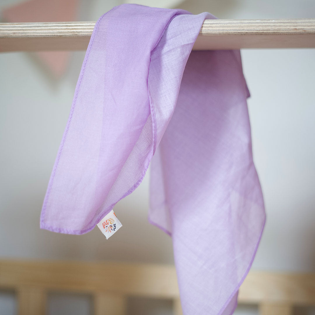 Een lila pit and play speeldoek van katoen hangt over een houten staaf.
