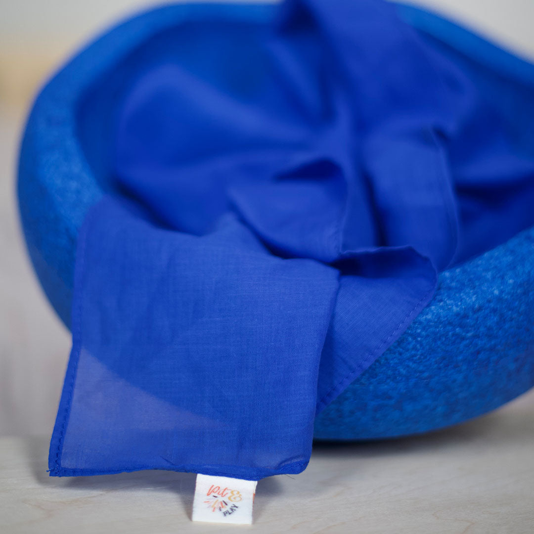 Een blauwe pit and play speeldoek ligt opgevouwen in een blauwe vilten kom.
