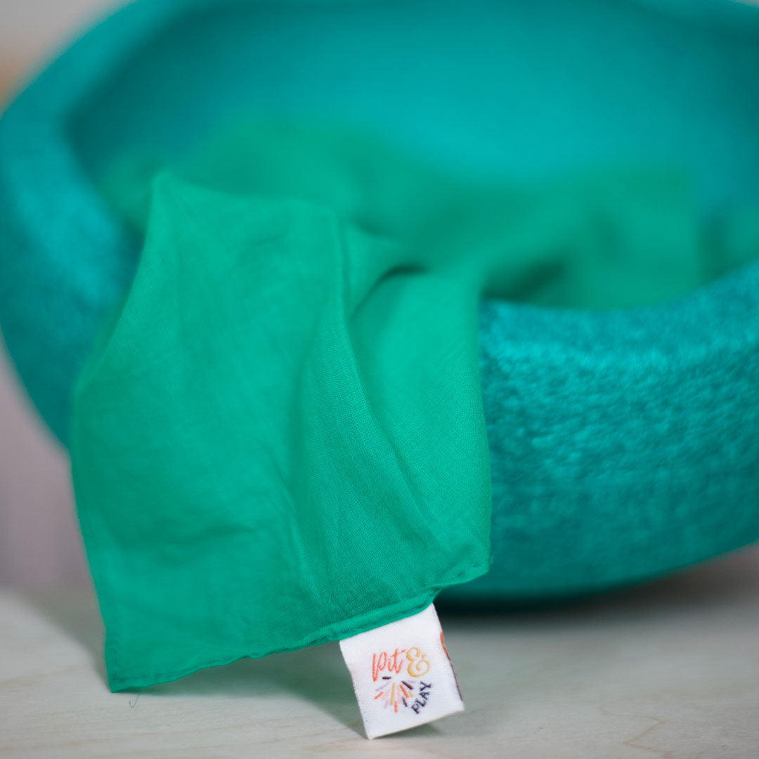 Detail van een groen pit and play speeldoek, deels in een groene vilten kom.