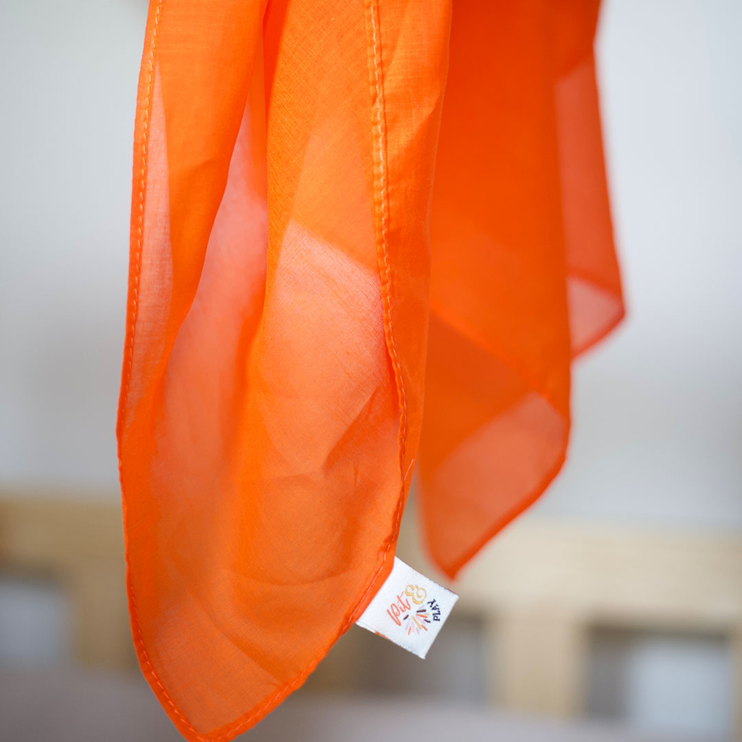 Een oranje pit and play speeldoek hangt, met het merklabel duidelijk zichtbaar.
