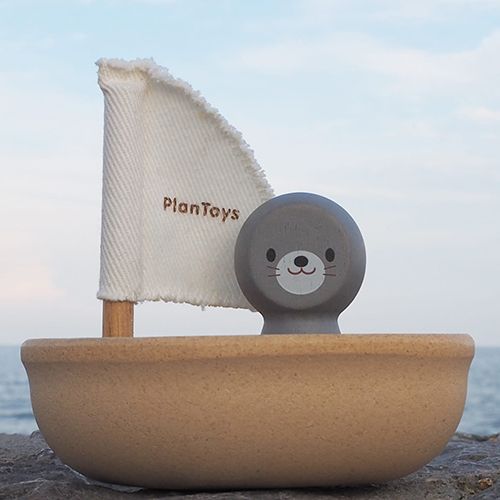Plan Toys badspeelgoed zeilbootje met zeehondje op een rots bij de zee.