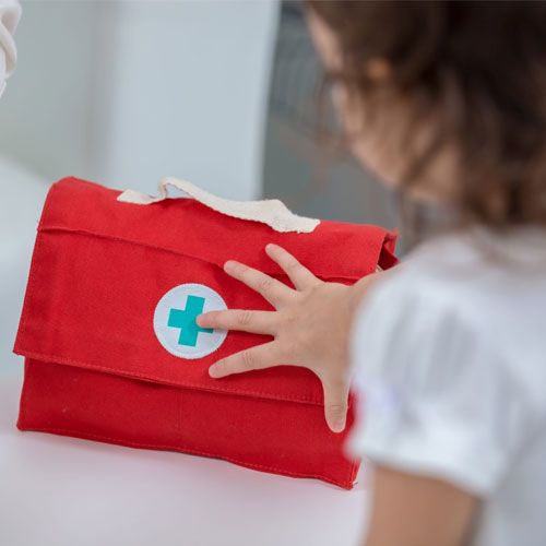 Een kinderhand reikt naar de rode dokterstas van de Plan Toys dokterspeelset.