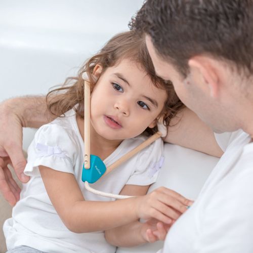 Een kind speelt dokter en draagt de stethoscoop van de Plan Toys dokterspeelset terwijl het naar een volwassene kijkt.