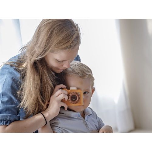 Een vrouw houdt een kind vast dat door de Plan Toys houten kaleidoscoop camera kijkt.