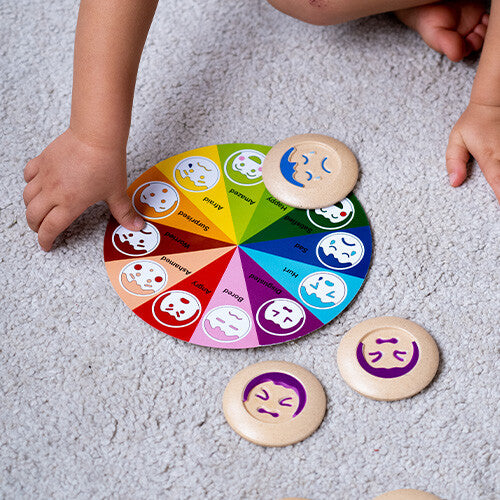 Een kind speelt met het Plan Toys educatieve memoriespel, waarbij een emotie-schijf op het kleurrijke bord wordt geplaatst.