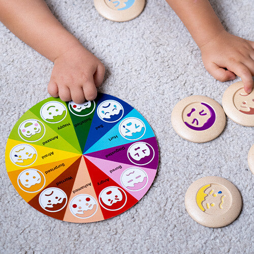Een kind speelt met het Plan Toys memoriespel met emotie-schijven op een grijze ondergrond.