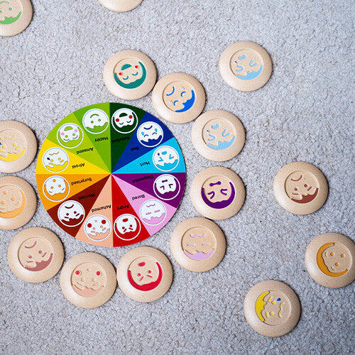 Overzicht van het complete Plan Toys houten memoriespel met alle emotie-schijven en het kleurrijke bord verspreid op een grijze ondergrond.