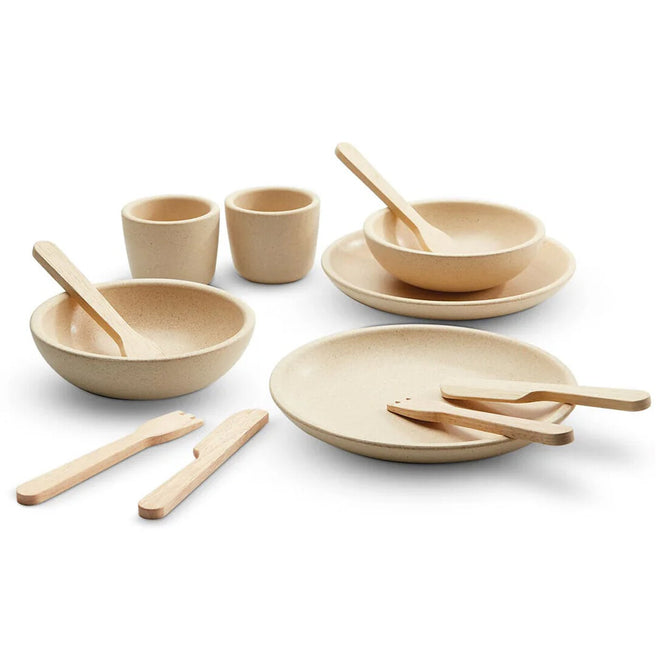 Plan Toys houten speelservies in beige kleur, bestaande uit borden, kommen, bekers en bestek.