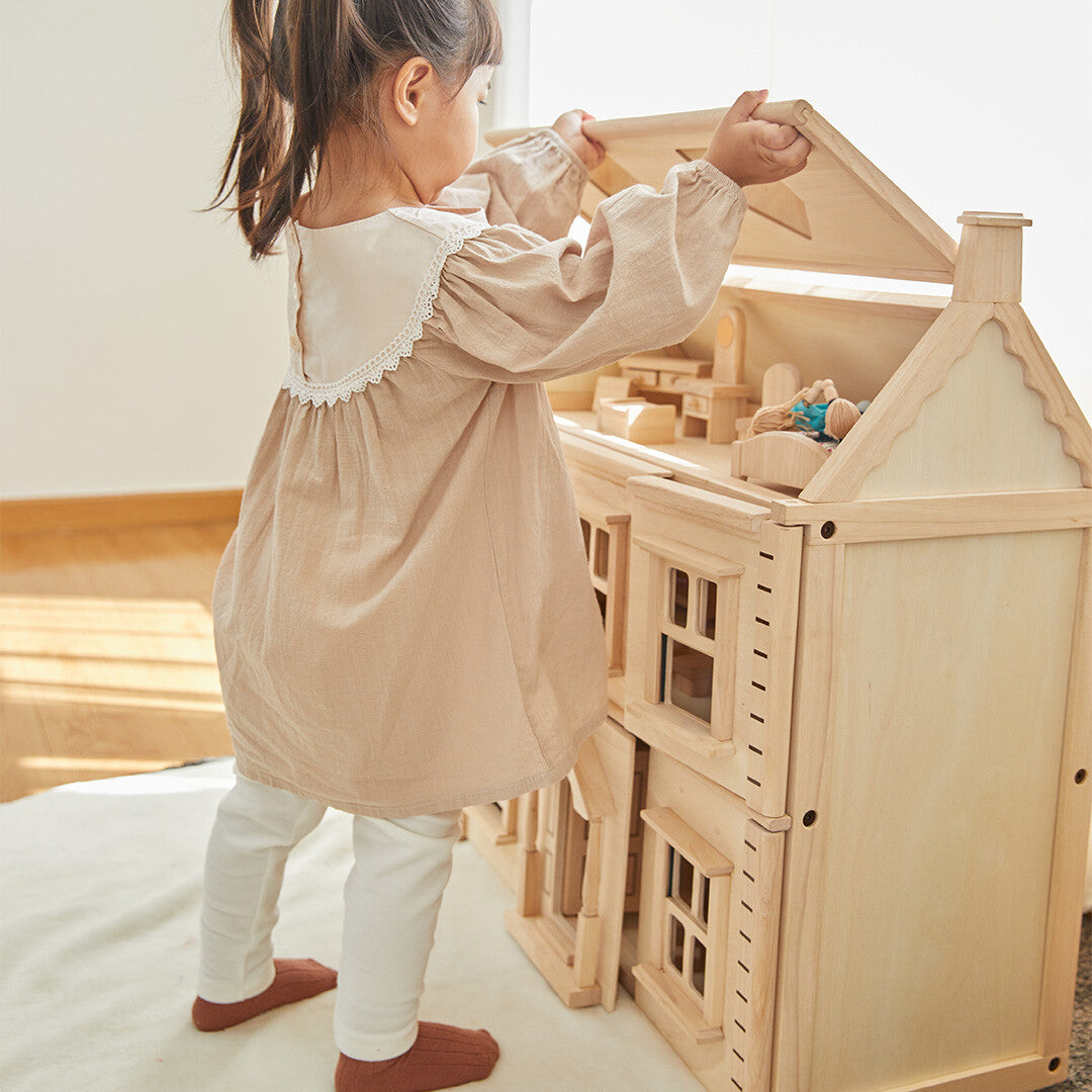 Kind staat en opent het dak van het Plan Toys Victoriaans houten poppenhuis.