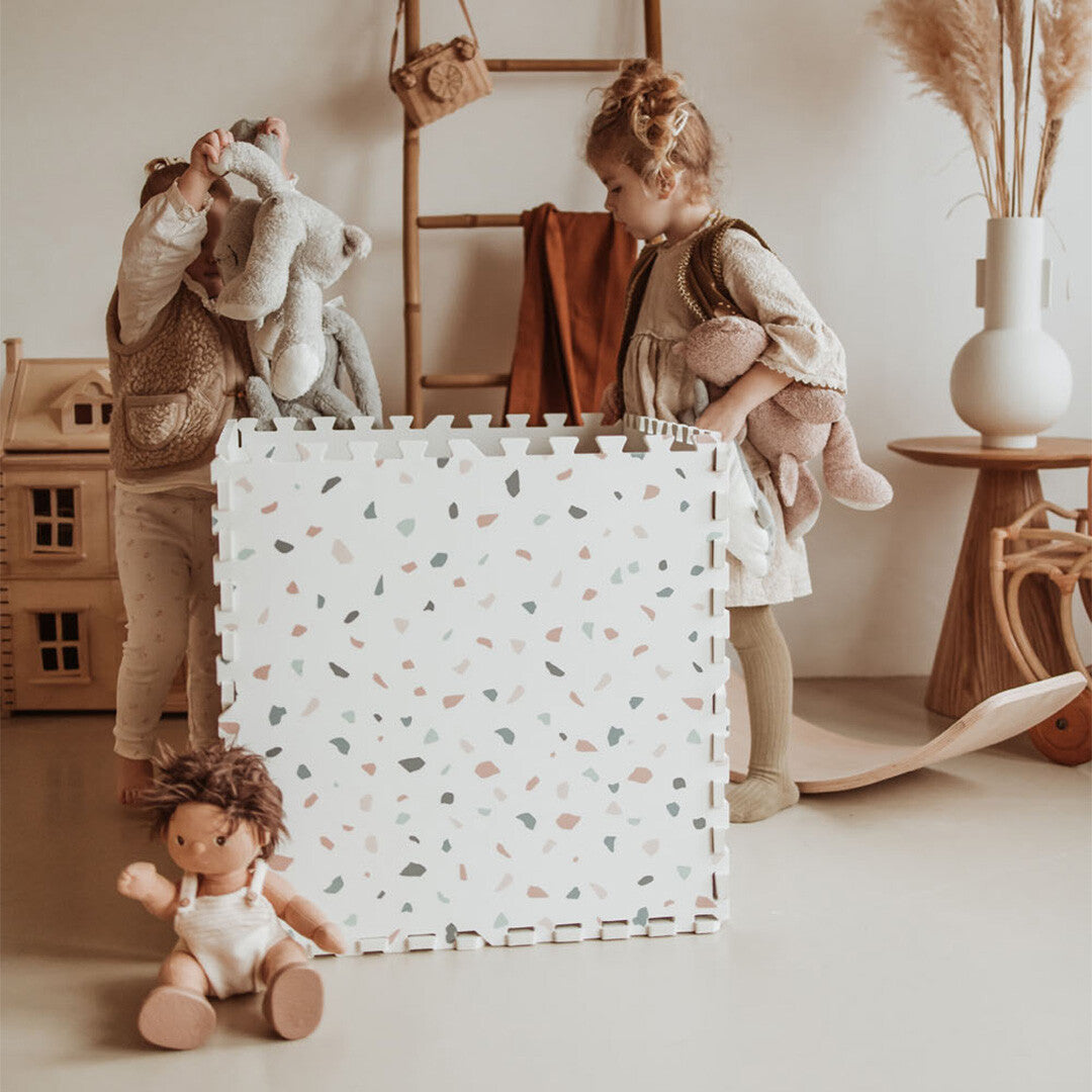 Twee kinderen staan bij een kubus gemaakt van play&go foam speelmat tegels met een willekeurig patroon.