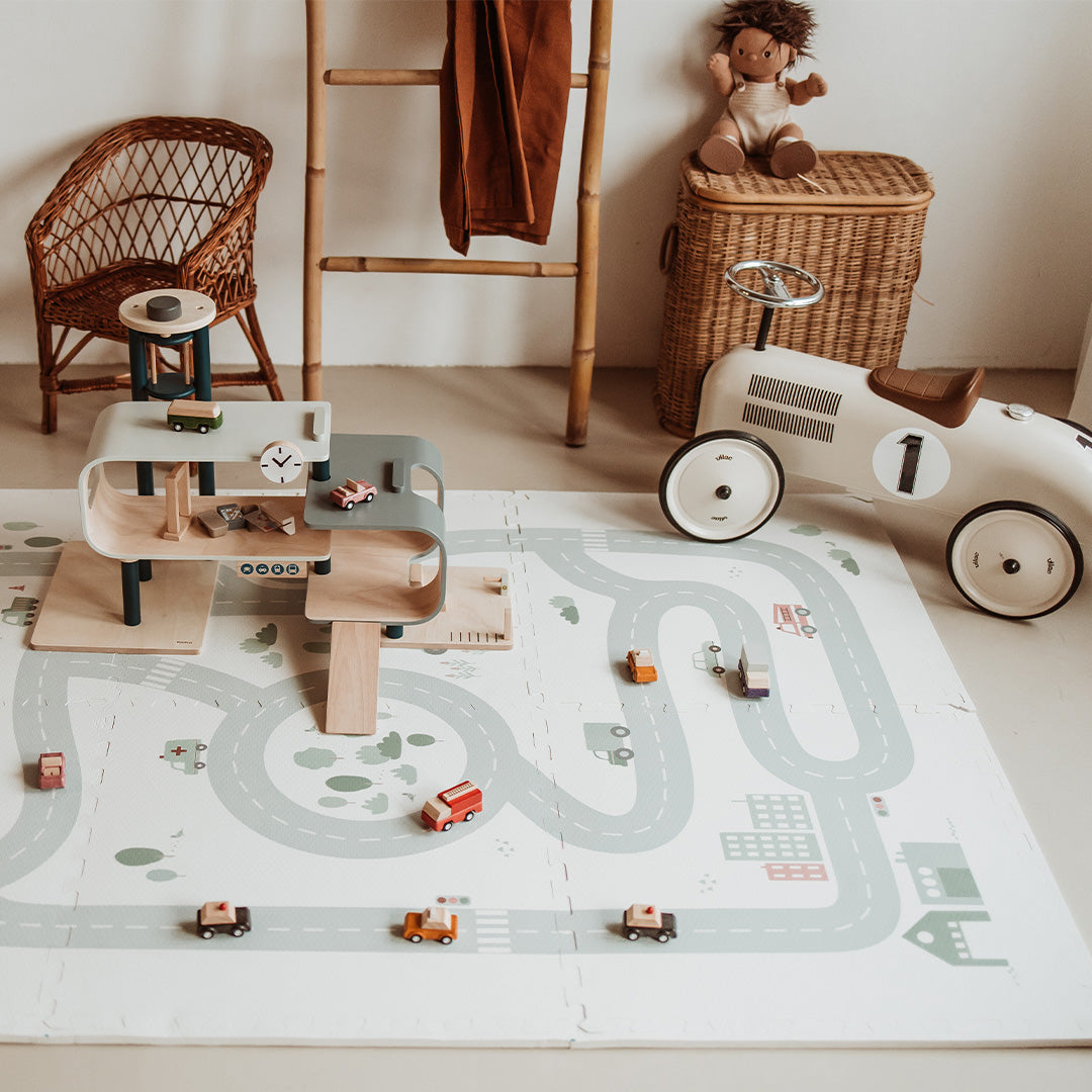 Een kinderspeelkamer met de play&go foam speelmat met wegenpatroon, een houten garage en speelgoedauto's.