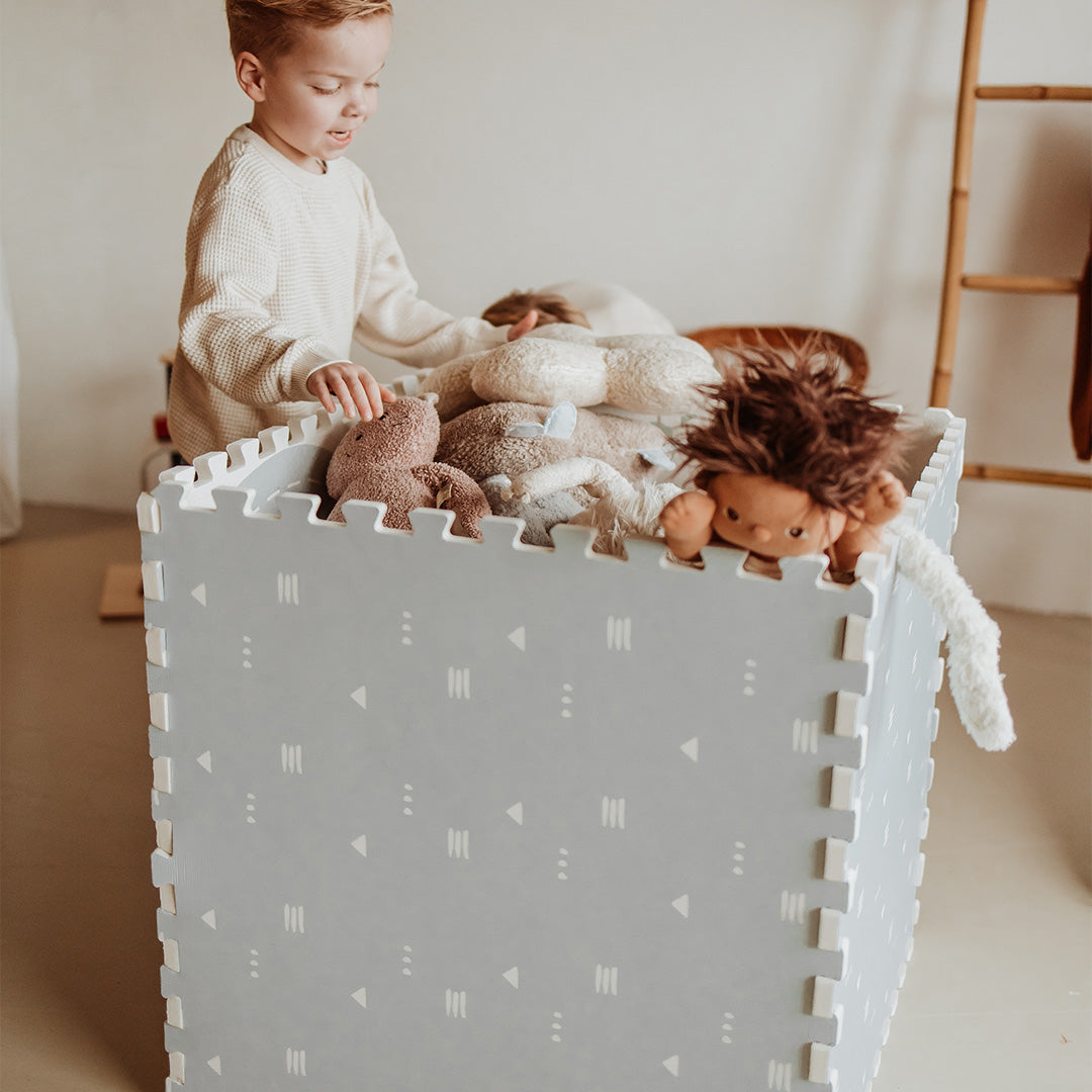Een kind stopt knuffels in een grijze opbergbox gemaakt van de play&go foam speelmat.
