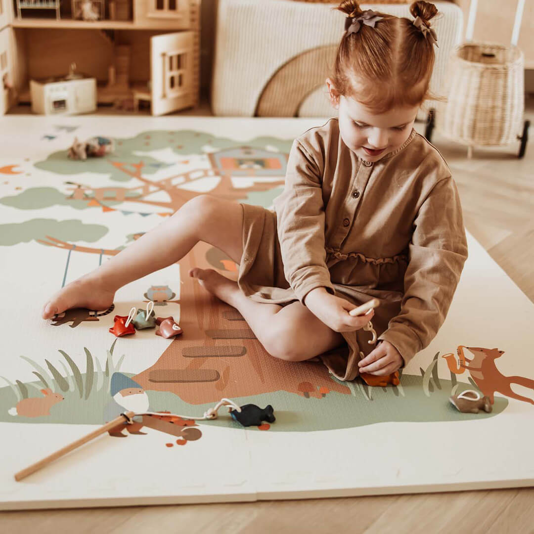 Een jong meisje speelt op de play&go foam speelmat met boomhutthema en houten speelgoed.