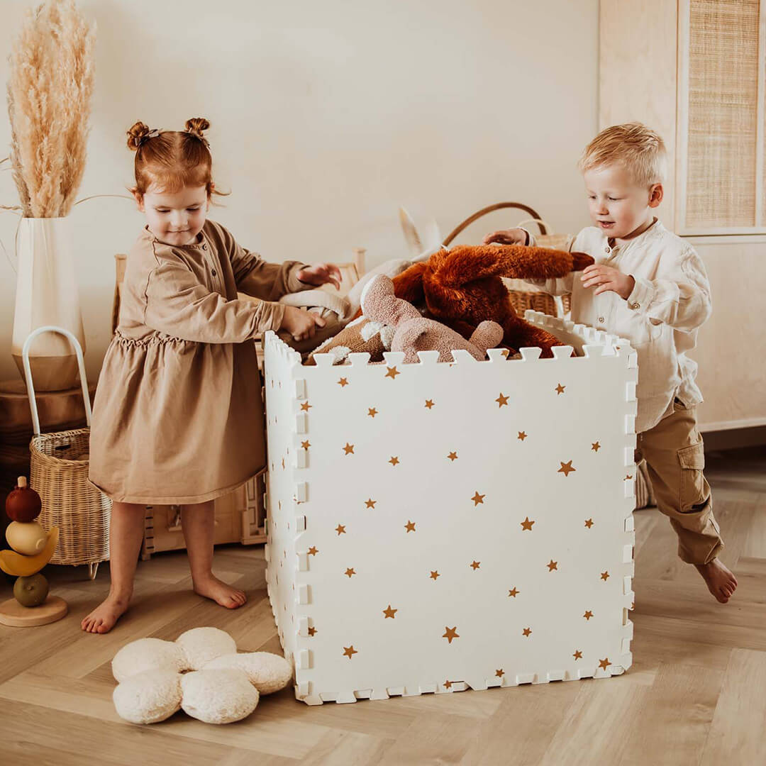 Twee kinderen staan bij een grote opbergbox gemaakt van de play&go foam speelmat met sterrenpatroon, gevuld met knuffels.