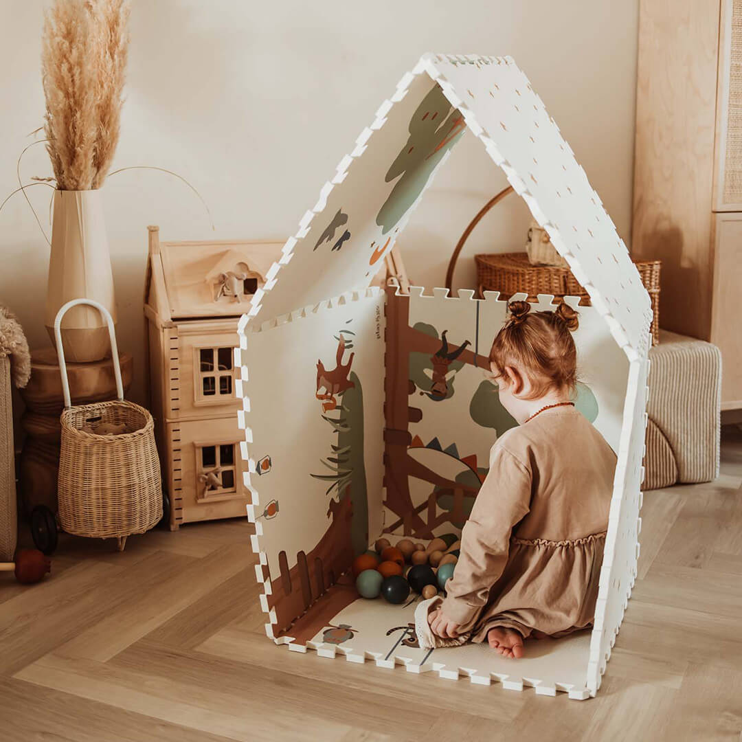 Een meisje zit in een speelhuisje gemaakt van de play&go foam speelmat met boomhutillustraties aan de binnenkant.