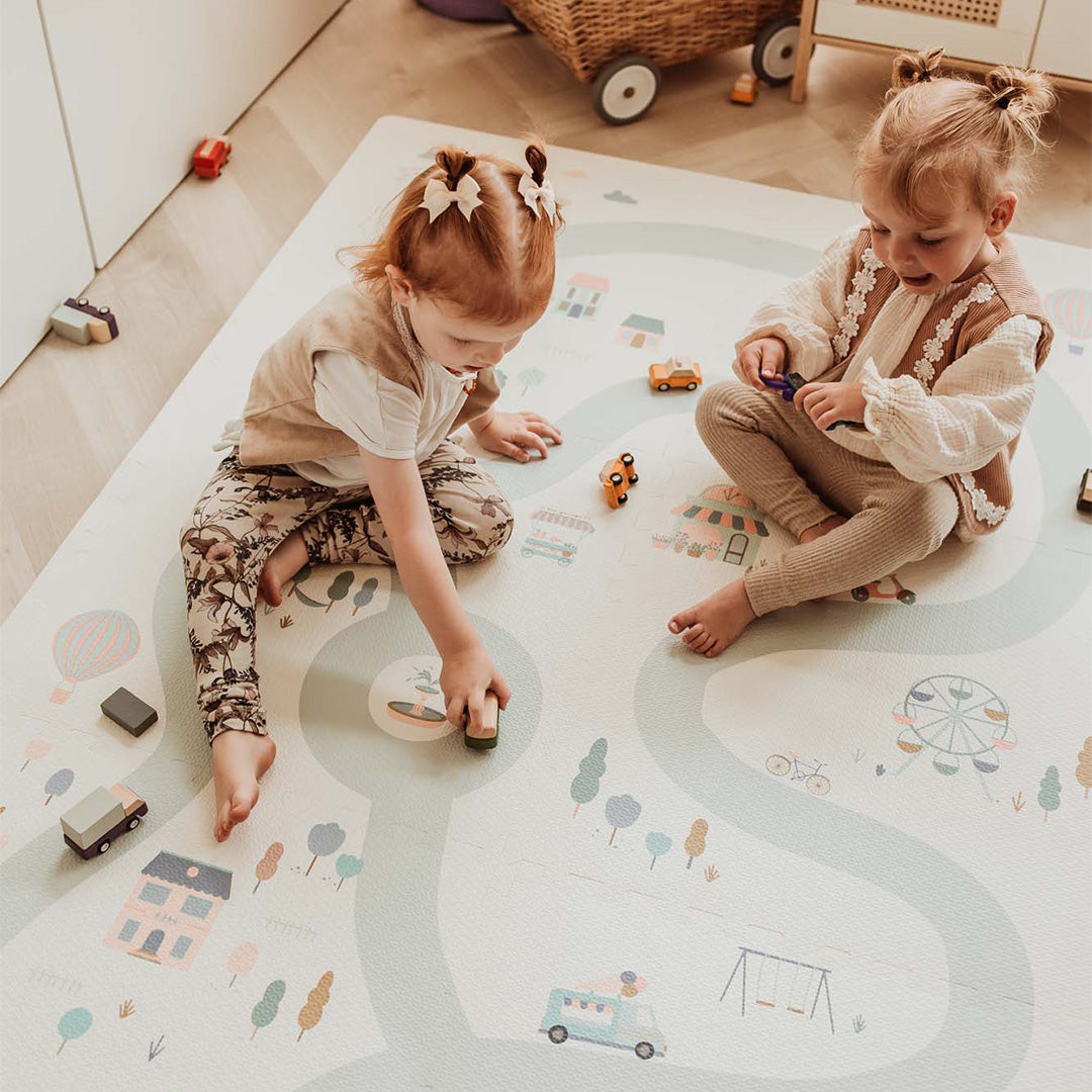 Twee peuters spelen met autootjes op de play&go foam speelmat met een dorpsthema.