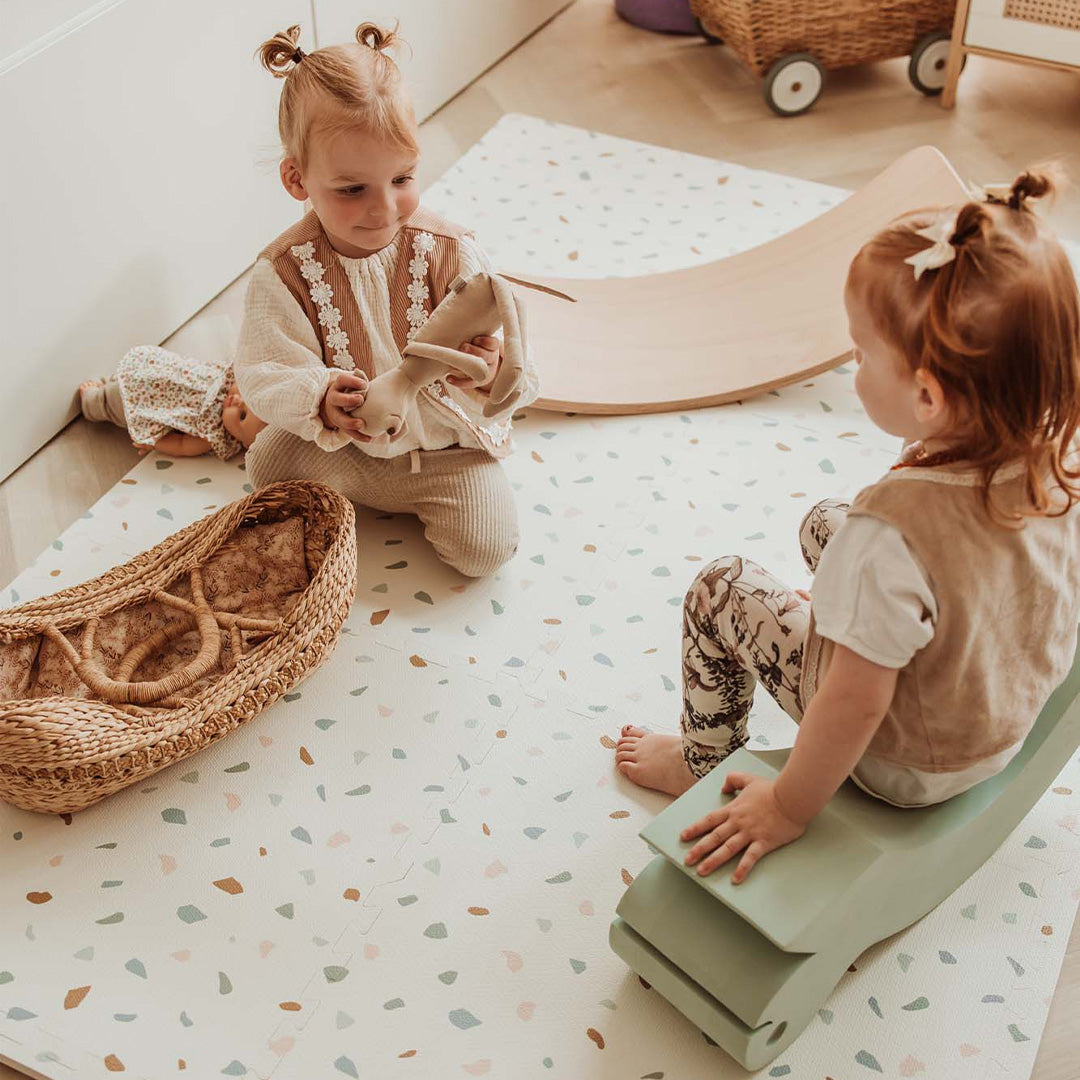Twee peuters zitten op de play&go foam speelmat met een abstract patroon van gekleurde vormen.