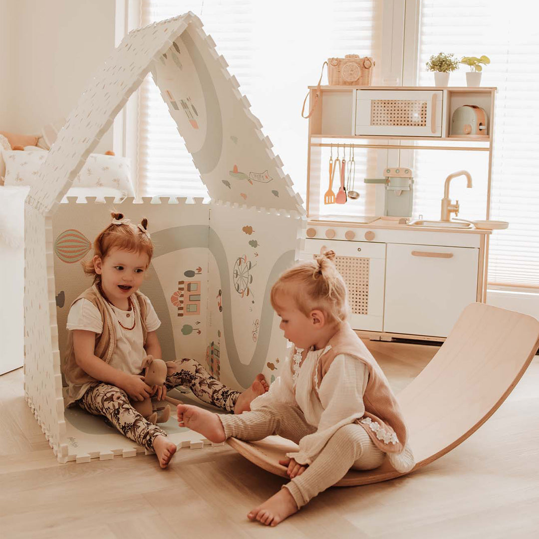 Twee peuters spelen in een speelhuis gemaakt van de play&go foam speelmat met een dorpsthema.