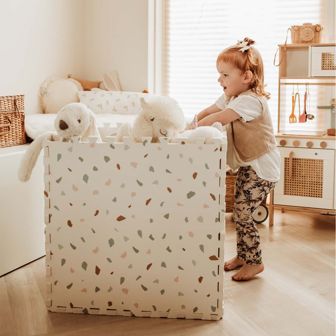 Een peuter staat naast een opbergbox gemaakt van de play&go foam speelmat met een abstract patroon.