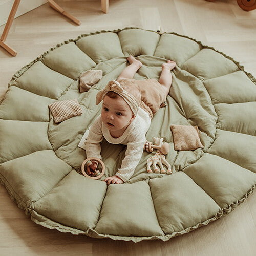 Een baby ligt op de buik op het uitgespreide play&go speelkleed coco in meadow green, met wat babyspeelgoed eromheen.