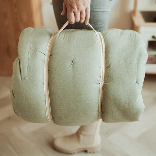 Een persoon draagt het opgerolde play&go speelkleed coco in meadow green, vastgezet met banden, als een draagbare tas.