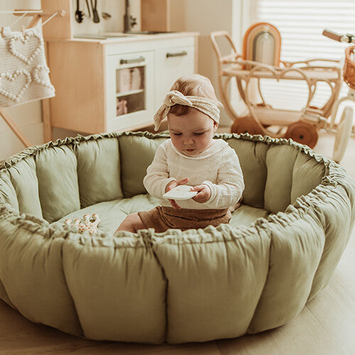 Een baby zit in het play&go speelkleed coco in meadow green, dat is opgetrokken tot een zacht, rond babynestje.