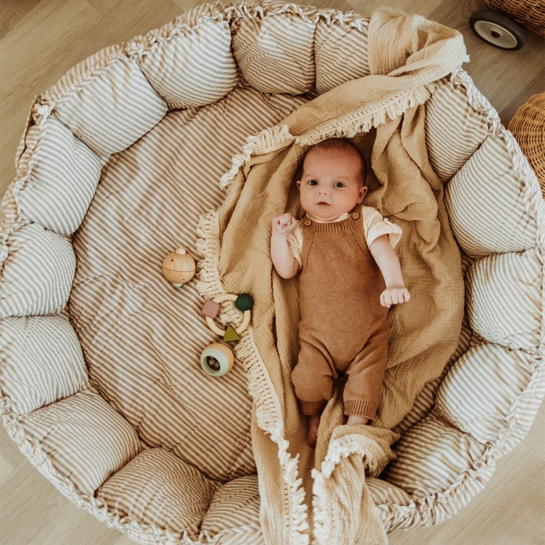 Baby ligt in het play&go 3-in-1 speelkleed dat als nestje is opgemaakt, met een deken en houten babyspeelgoed.