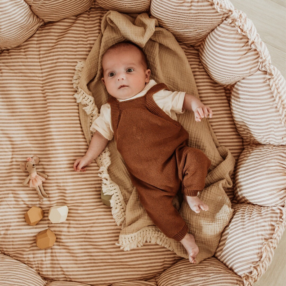 Baby ligt op een gestreept bruin play&go babyspeelkleed dat als babynestje is gevormd.