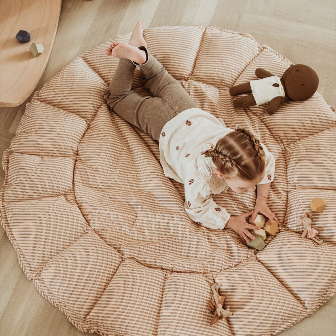 Kind speelt met houten blokken op een uitgespreid rond play&go speelkleed met bruine strepen.