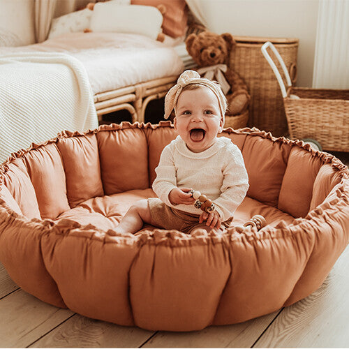Een lachende baby zit in het play&go 3-in-1 speelkleed in tawny brown, opgesteld als een babynestje.