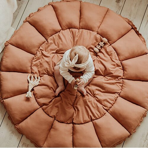 Een baby zit op het play&go 3-in-1 speelkleed in tawny brown, plat uitgespreid op de vloer.