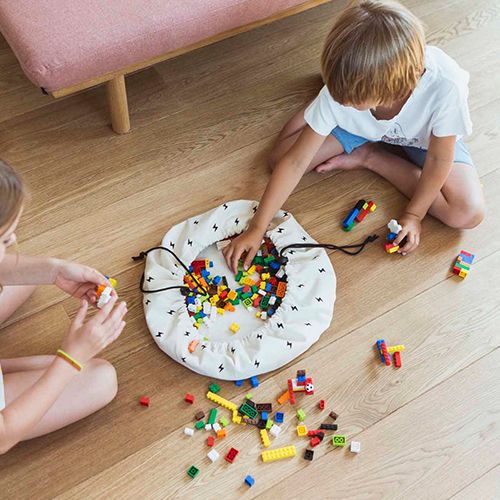 Twee kinderen spelen met bouwblokken op een houten vloer, met de play&go opbergzak als speelmat.