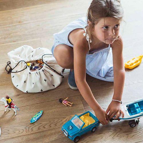 Een meisje speelt met klein speelgoed op een houten vloer naast een open play&go opbergzak met thunderstrike patroon.