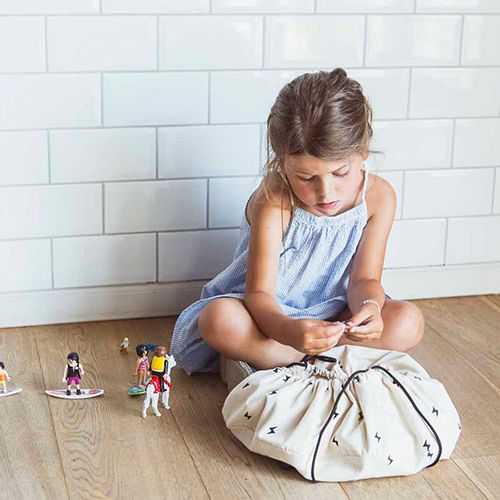 Een meisje speelt met kleine figuren op een houten vloer naast een deels gesloten play&go opbergzak met thunderstrike patroon.