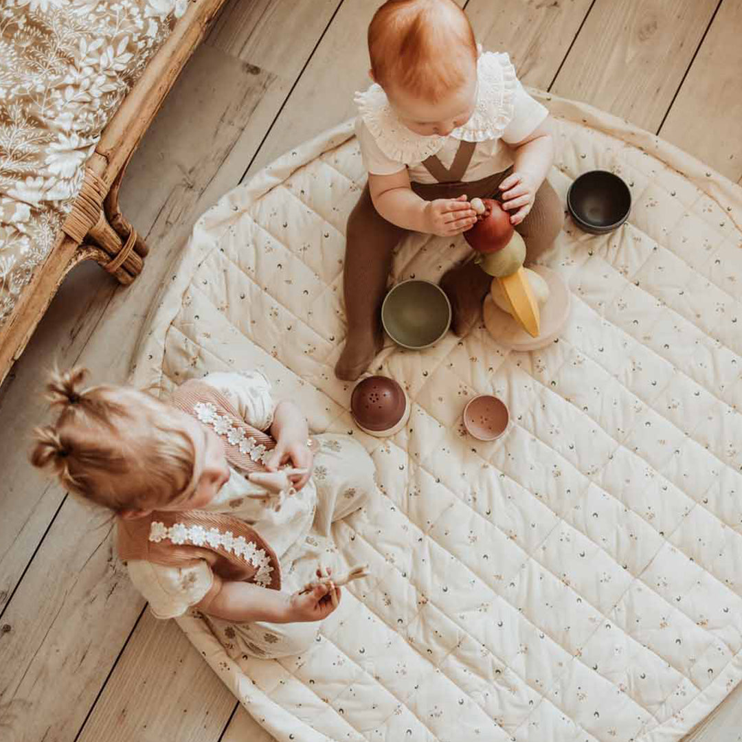 Twee baby's zitten op het play&go ronde babyspeelkleed en spelen met speelgoed.