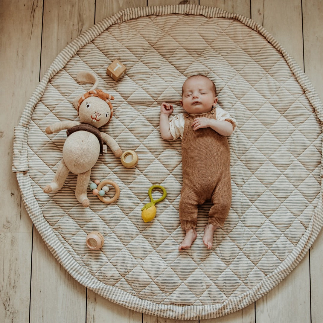 Een slapende baby ligt op het ronde, gestreepte play&go baby speelkleed met speelgoed eromheen.