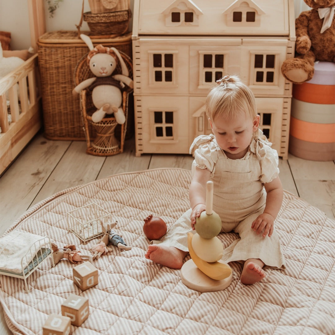 Een baby speelt op het play&go gestreepte speelkleed met een houten stapeltoren.