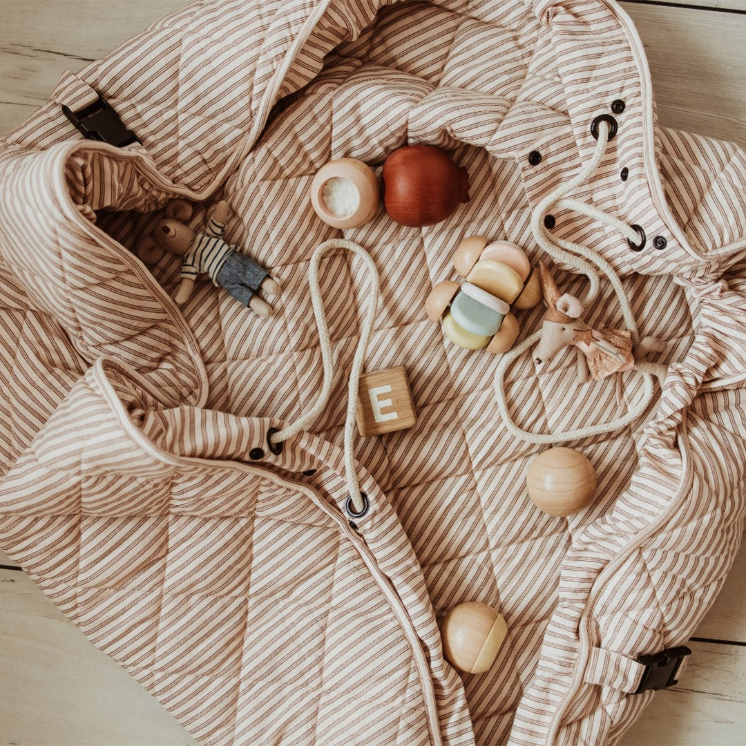 Het play&go gestreepte speelkleed ligt deels opgevouwen met diverse houten speeltjes en een trekkoord.