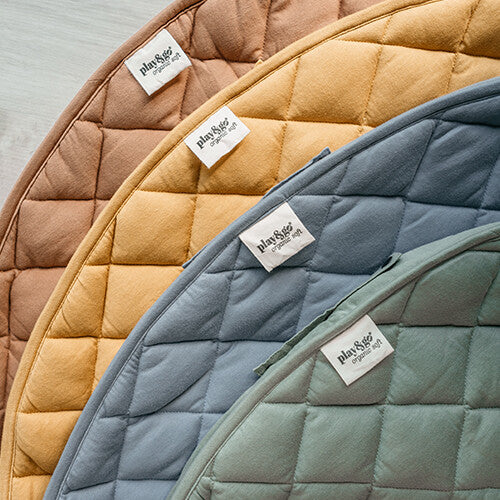 Play&go collectie van vier gestapelde, gewatteerde babyspeelkleden in verschillende kleuren met 'organic soft' label.