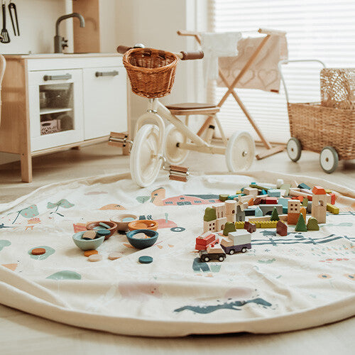 Een play&go speelkleed met boerderijthema ligt uitgevouwen op de vloer met houten speelgoed erop.