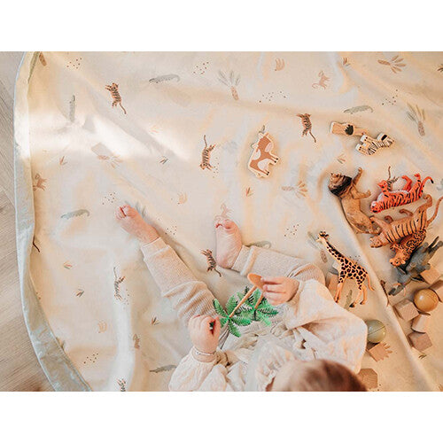 Een baby ligt op het play&go speelkleed met jungleprint en speelgoeddieren.