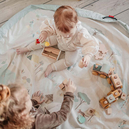 Twee kinderen spelen op het play&go speelkleed met houten blokken en een trein.