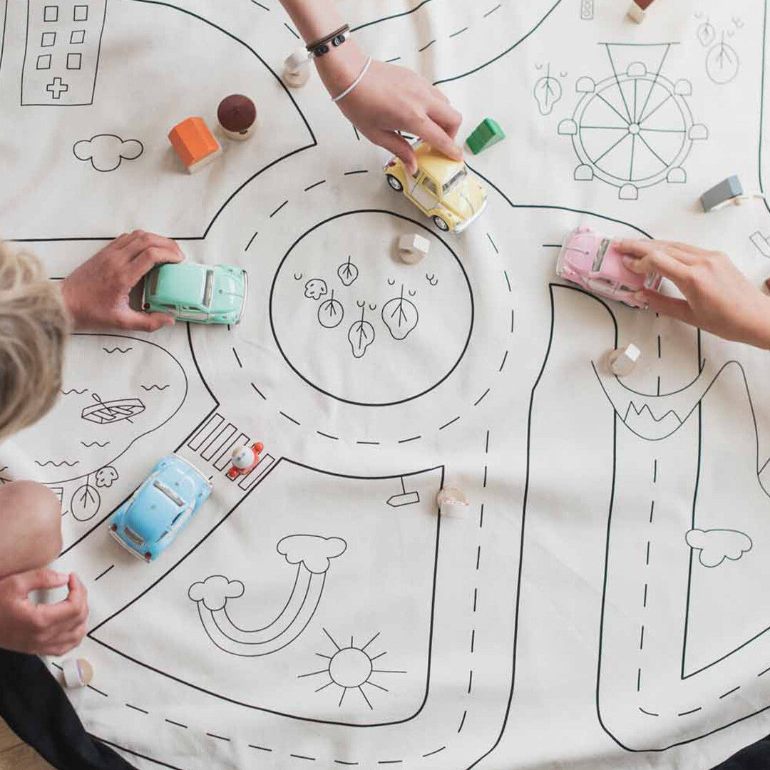 Kinderhanden spelen met speelgoedauto's en houten blokken op het play&go speelkleed met wegenpatroon.