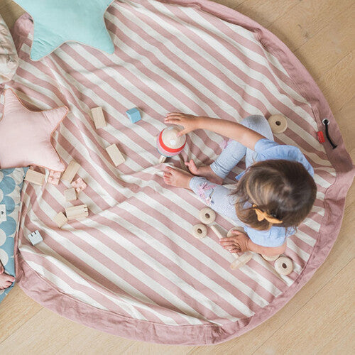 Kind speelt op een play&go speelkleed met roze en witte strepen, omringd door houten speelgoed.