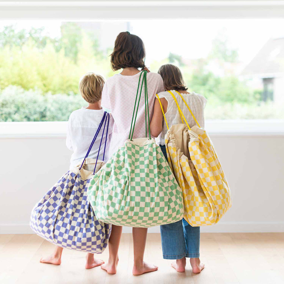Drie kinderen dragen play&go geruite opbergzakken in blauw, groen en geel over hun schouders.