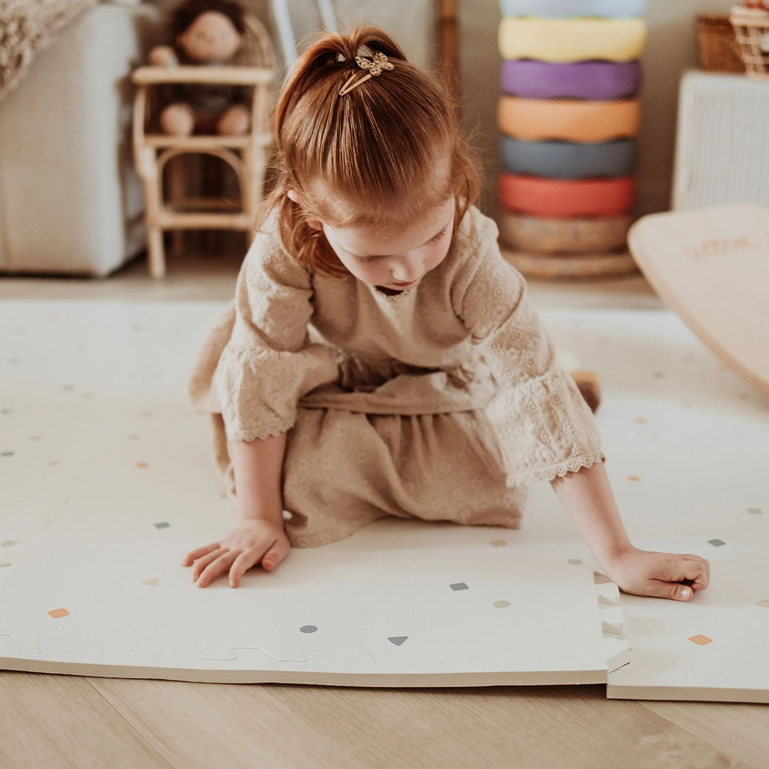 Een kind speelt op een play&go foam speelmat met een patroon van gekleurde stippen en vormen.