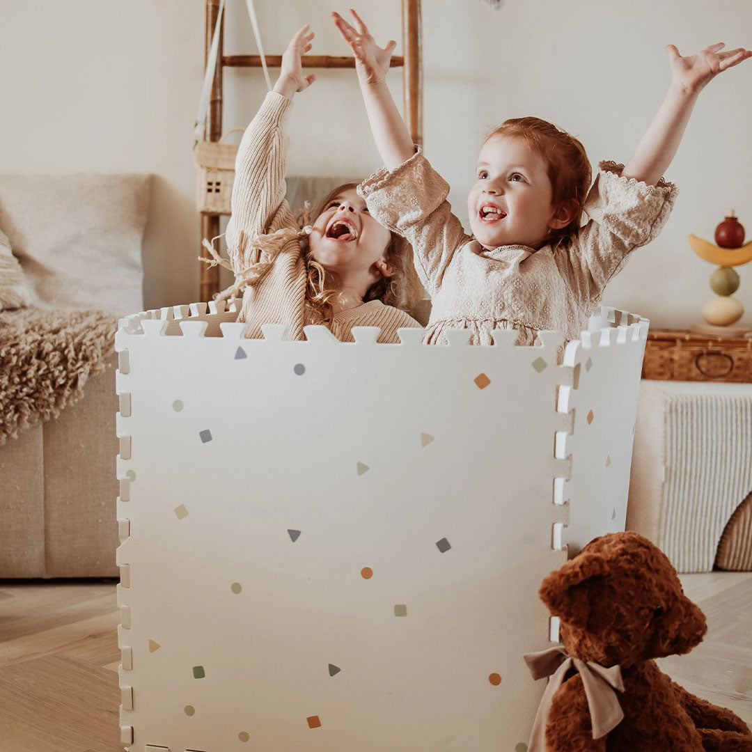 Twee lachende kinderen spelen in een kubusvormige constructie gemaakt van play&go foam speelmat tegels met stippenpatroon.