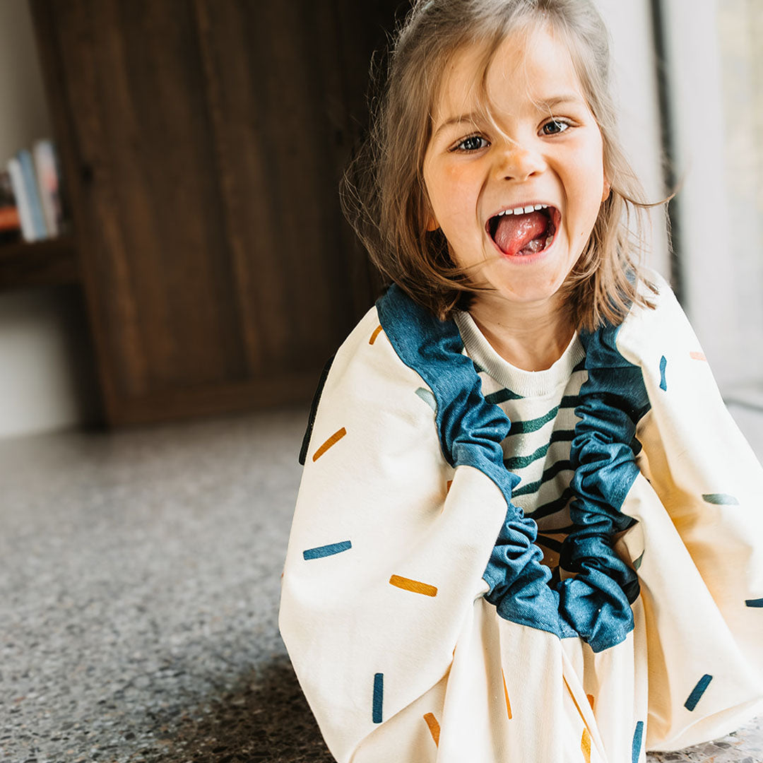 Een lachend kind met het play&go speelkleed en opbergzak met confetti-patroon om haar schouders.