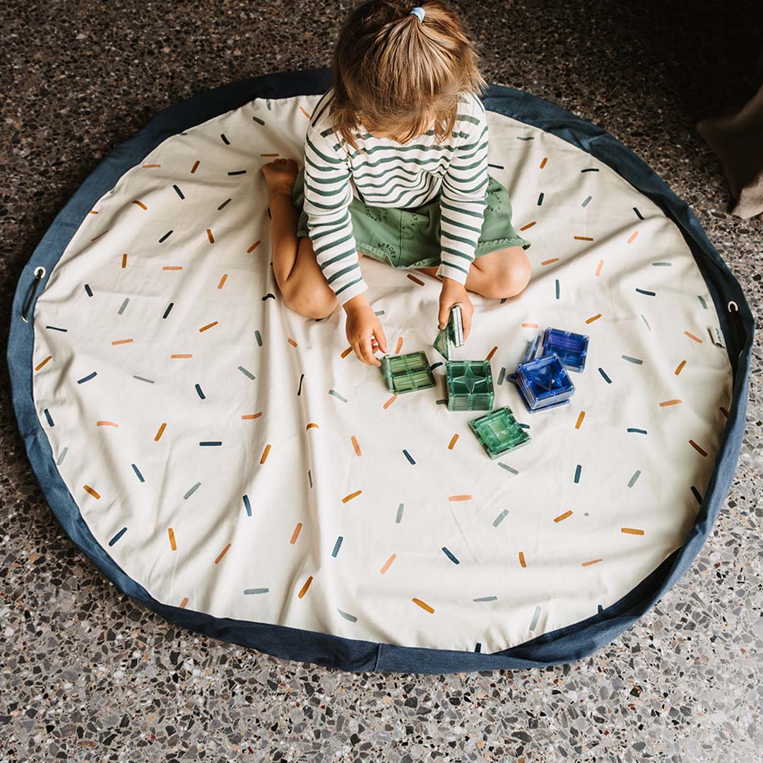 Een kind speelt op het uitgespreide play&go speelkleed met confetti-patroon.