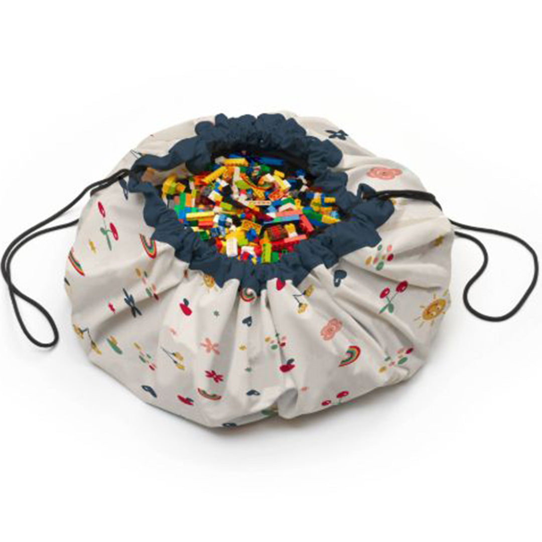 play&go speelkleed en opbergzak met bloemen, harten en regenbogen, dichtgetrokken en gevuld met kleurrijke bouwblokken.